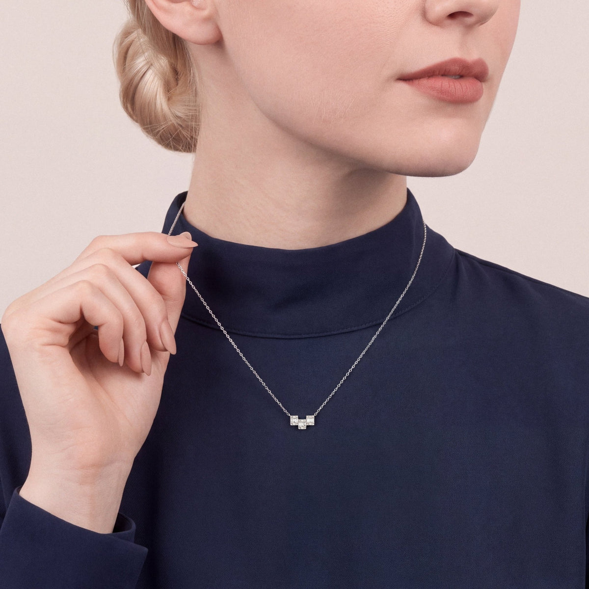 Woman in a navy mock-neck top lifting the chain of a natural diamond baguette geometric bar necklace in 18K white gold
