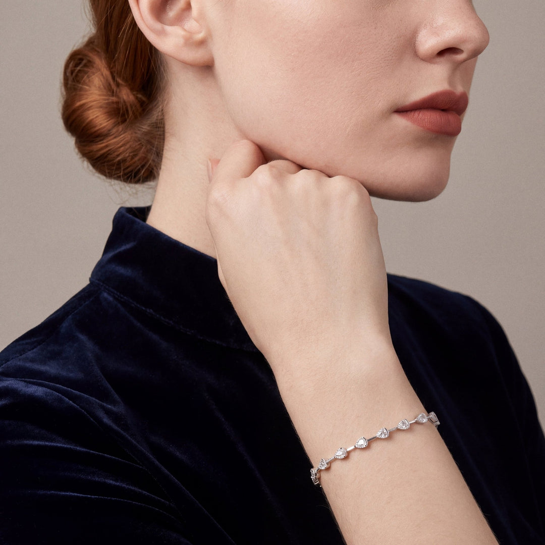 Woman in a navy velvet stand-collar top wearing a natural diamond baguette teardrop station bracelet in 14K white gold, fist resting at the jaw