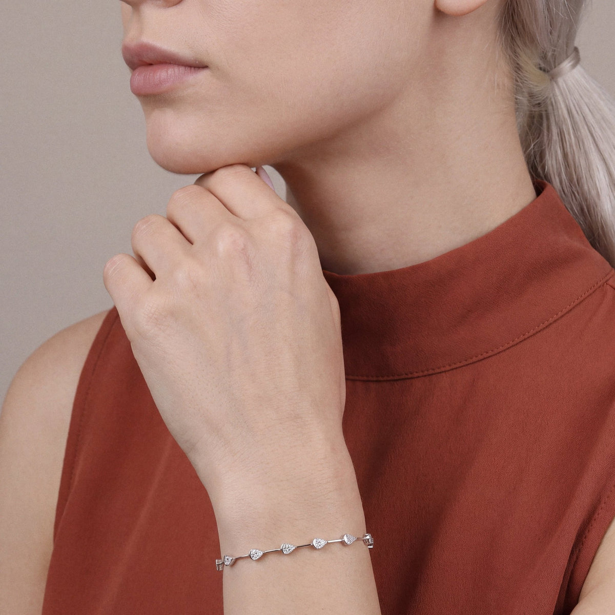 Woman in a rust mock-neck top wearing a natural diamond baguette teardrop station bracelet in 14K white gold, fingers at the chin