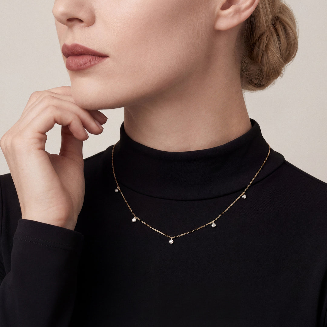 Woman in a black mock-neck top wearing a natural diamond bezel drop station necklace in 14K yellow and white gold