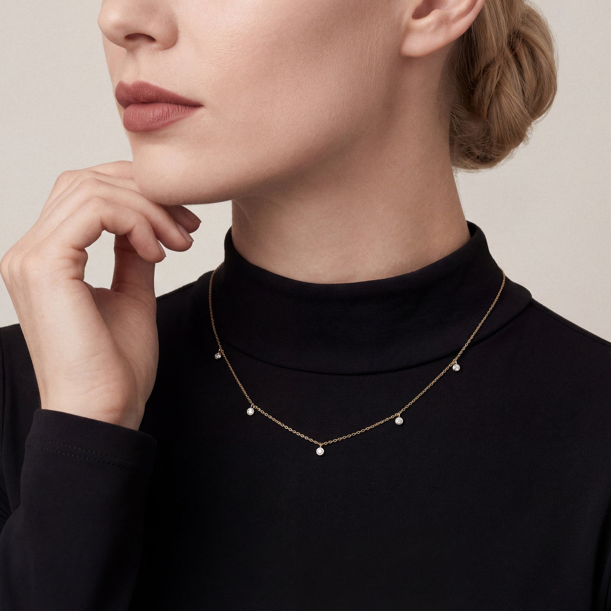 Woman in a black mock-neck top wearing a natural diamond bezel drop station necklace in 14K yellow and white gold
