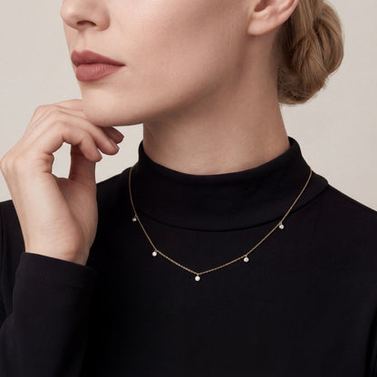Woman in a black mock-neck top wearing a natural diamond bezel drop station necklace in 14K yellow and white gold