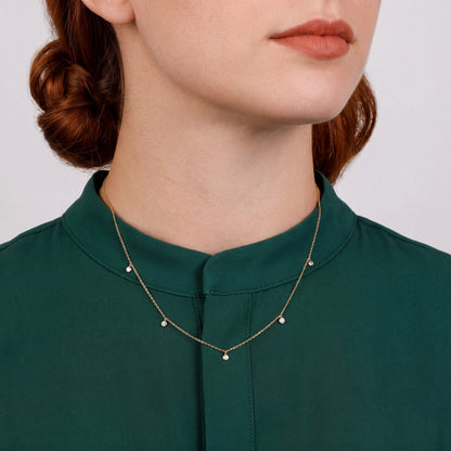 Woman in an emerald stand-collar blouse wearing a natural diamond bezel drop station necklace in 14K yellow and white gold