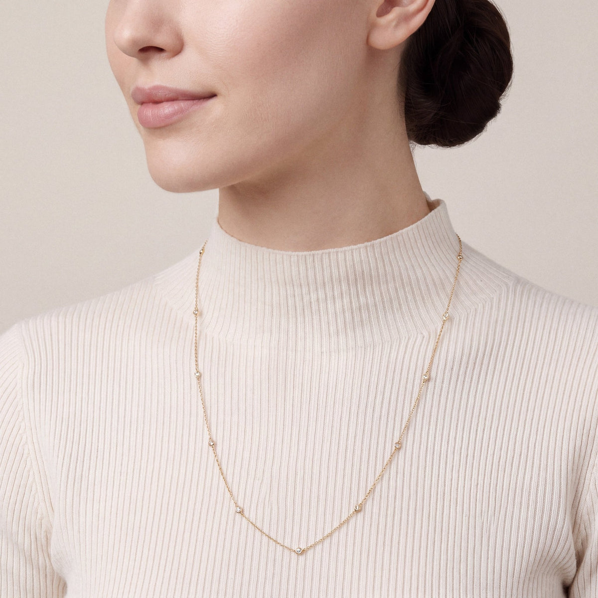 Woman in an ivory ribbed cashmere funnel-neck top wearing a 0.26 ct tw natural diamond bezel station necklace in 14K yellow gold