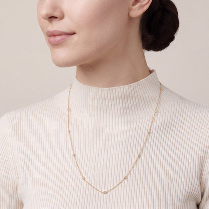 Woman in an ivory ribbed cashmere funnel-neck top wearing a 0.26 ct tw natural diamond bezel station necklace in 14K yellow gold