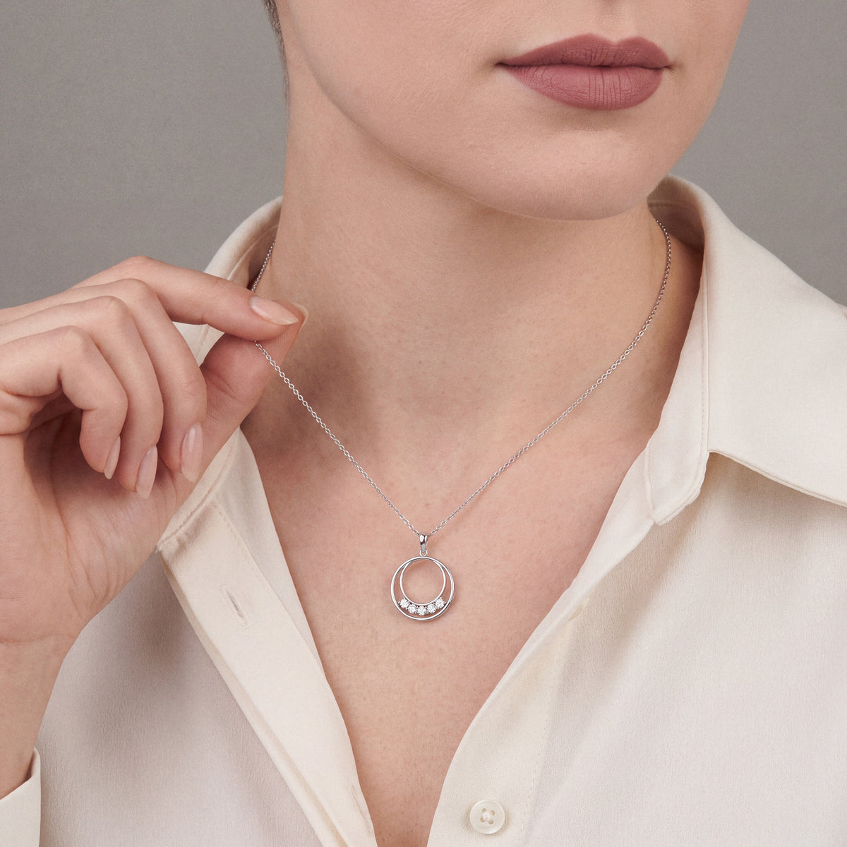 Woman in an ivory silk shirt wearing the natural diamond double circle pendant necklace in 14K white gold