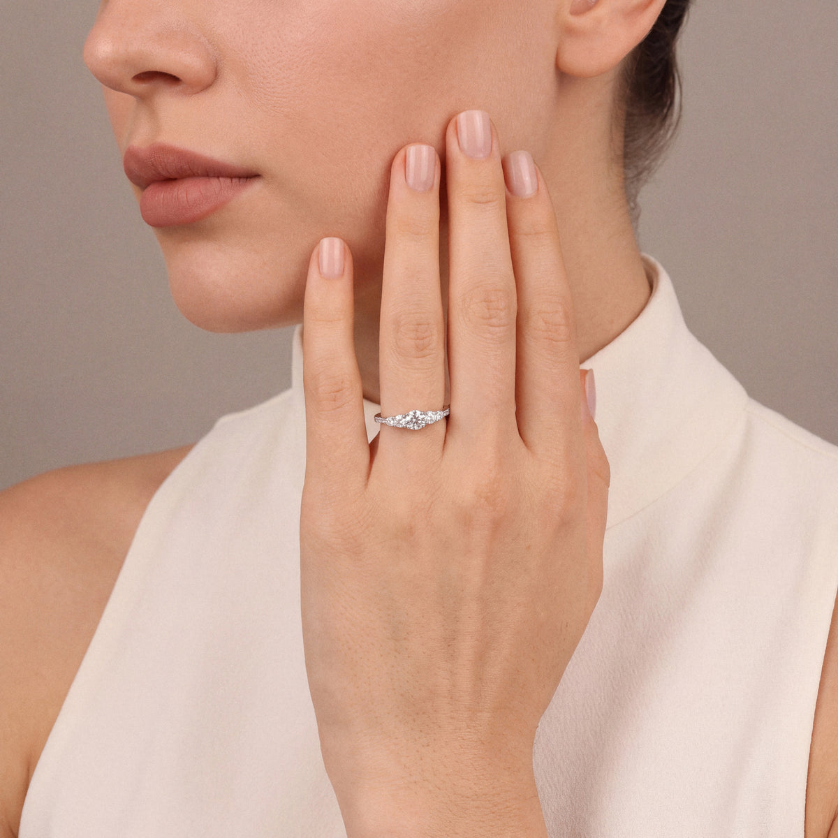 Natural diamond five-stone ring in 14K white gold worn on the ring finger, hand at the cheek, ivory high-neck top
