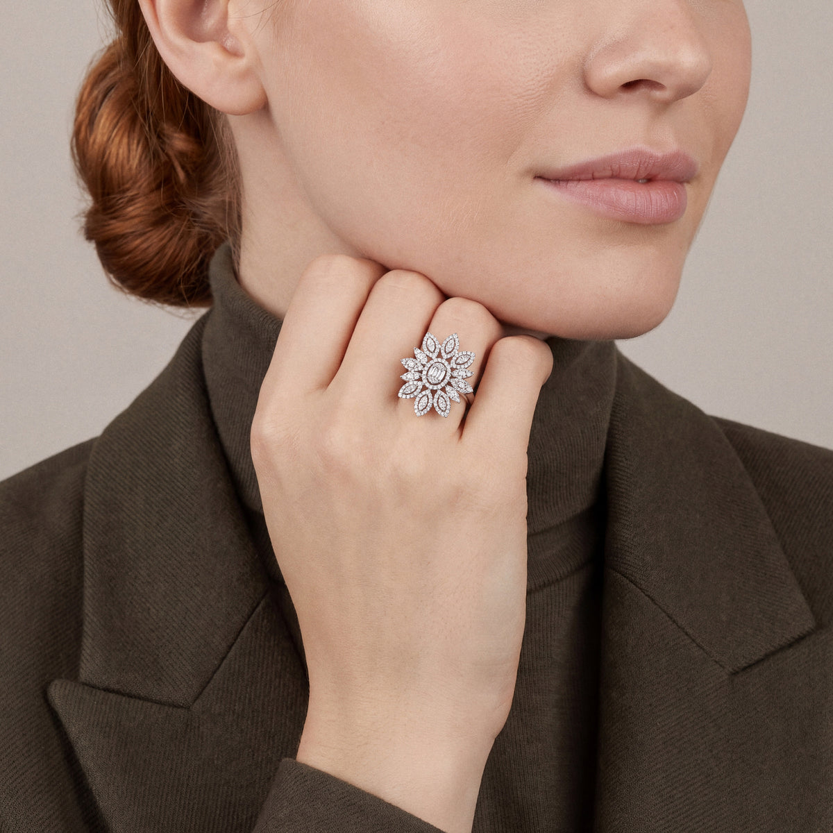 Woman in an olive blazer and turtleneck wearing a 1.59 ct natural diamond flower cocktail ring in 14K white gold on the ring finger, folded fingers under the chin