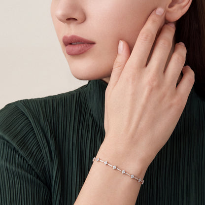 Woman in a forest-green plisse top wearing a natural diamond flower tennis bracelet in 14K rose and white gold, fingertips at the jaw