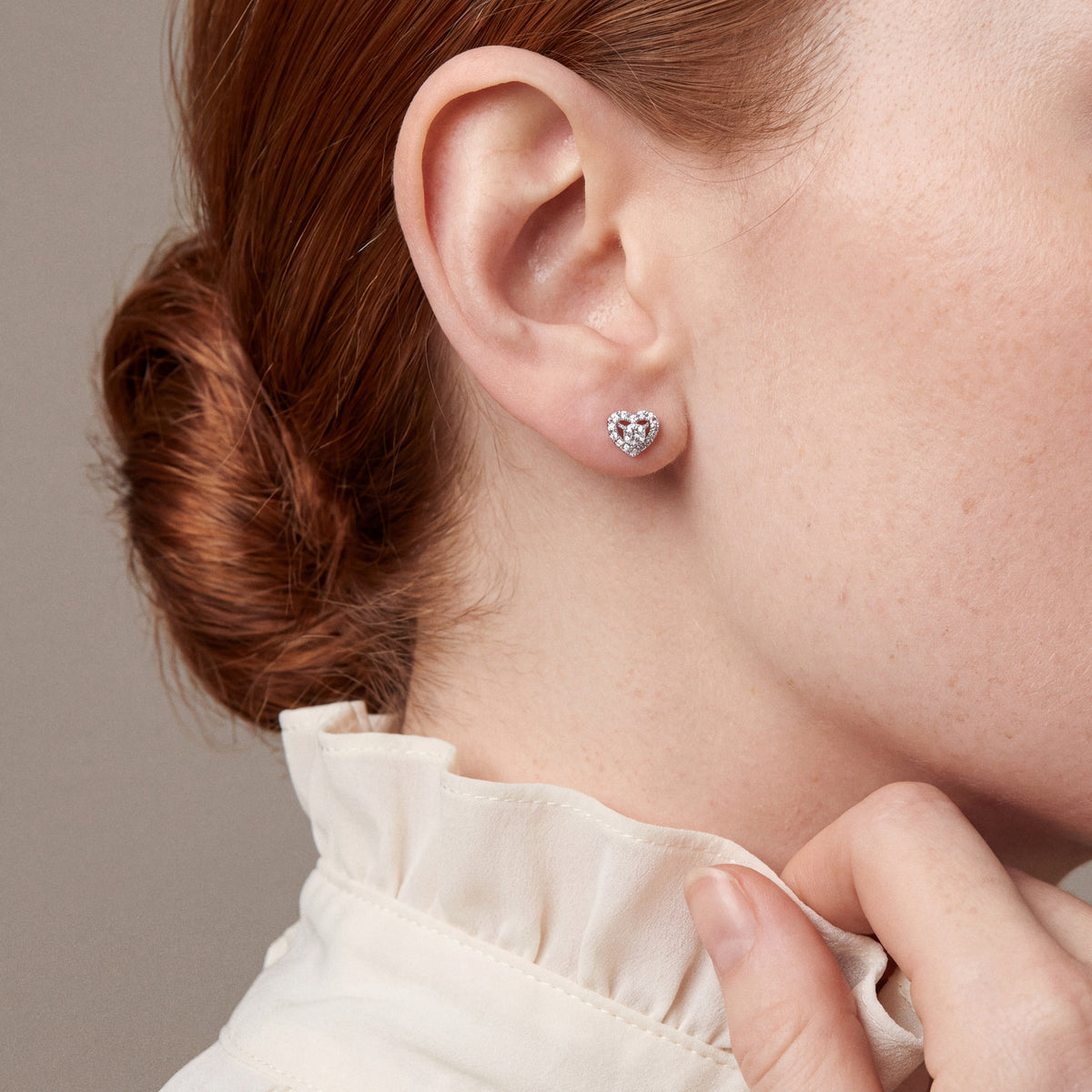 Natural diamond heart halo stud earring in 18K white gold, worn with an ivory ruffled silk collar