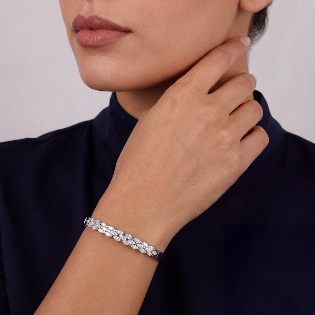 Woman in a navy high-neck top wearing a natural diamond marquise bangle in 18K white gold, fingertips at the jaw