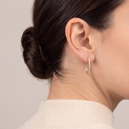 Model in a cream ribbed cashmere high neck, turned away, wearing a natural diamond oval J hoop earring in 14K rose gold