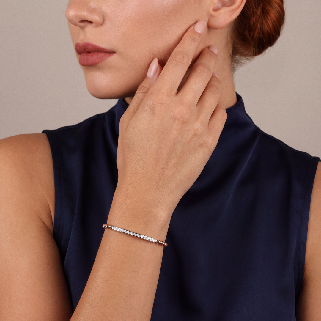 Woman in a midnight-navy high-neck top, hand at her cheek, wearing a natural diamond pavé bar bead bracelet in 14K rose and white gold