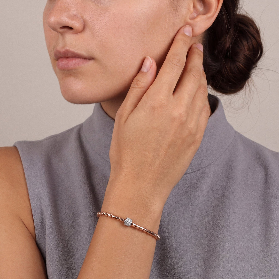 Woman in a dove-grey sleeveless funnel-neck top, hand at her cheek, wearing the natural diamond pavé barrel bead bracelet in 14K rose and white gold