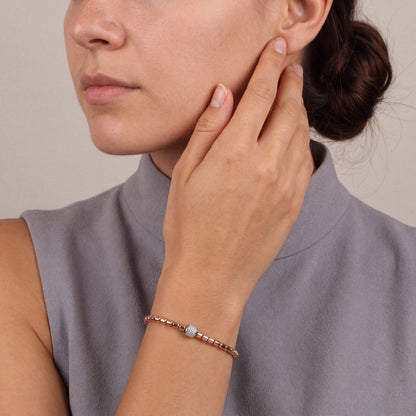 Woman in a dove-grey sleeveless funnel-neck top, hand at her cheek, wearing the natural diamond pavé barrel bead bracelet in 14K rose and white gold
