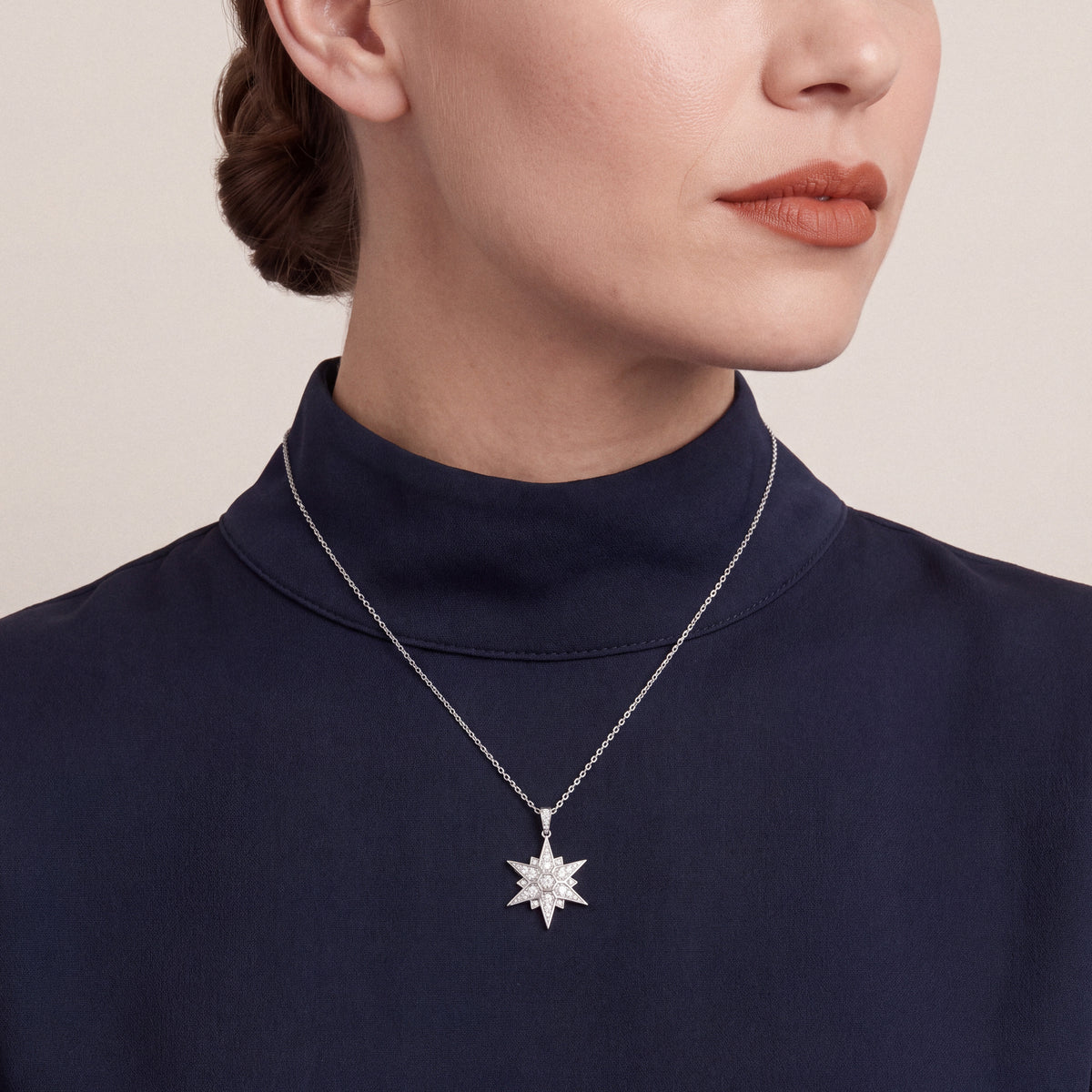 Woman in a navy funnel-neck top wearing the natural diamond pavé starburst pendant necklace in 14K white gold