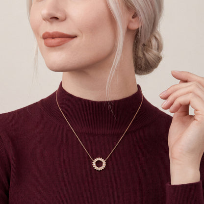 Woman in a burgundy rib-knit mock-neck top wearing a natural diamond petal circle pendant necklace in 14K rose gold.