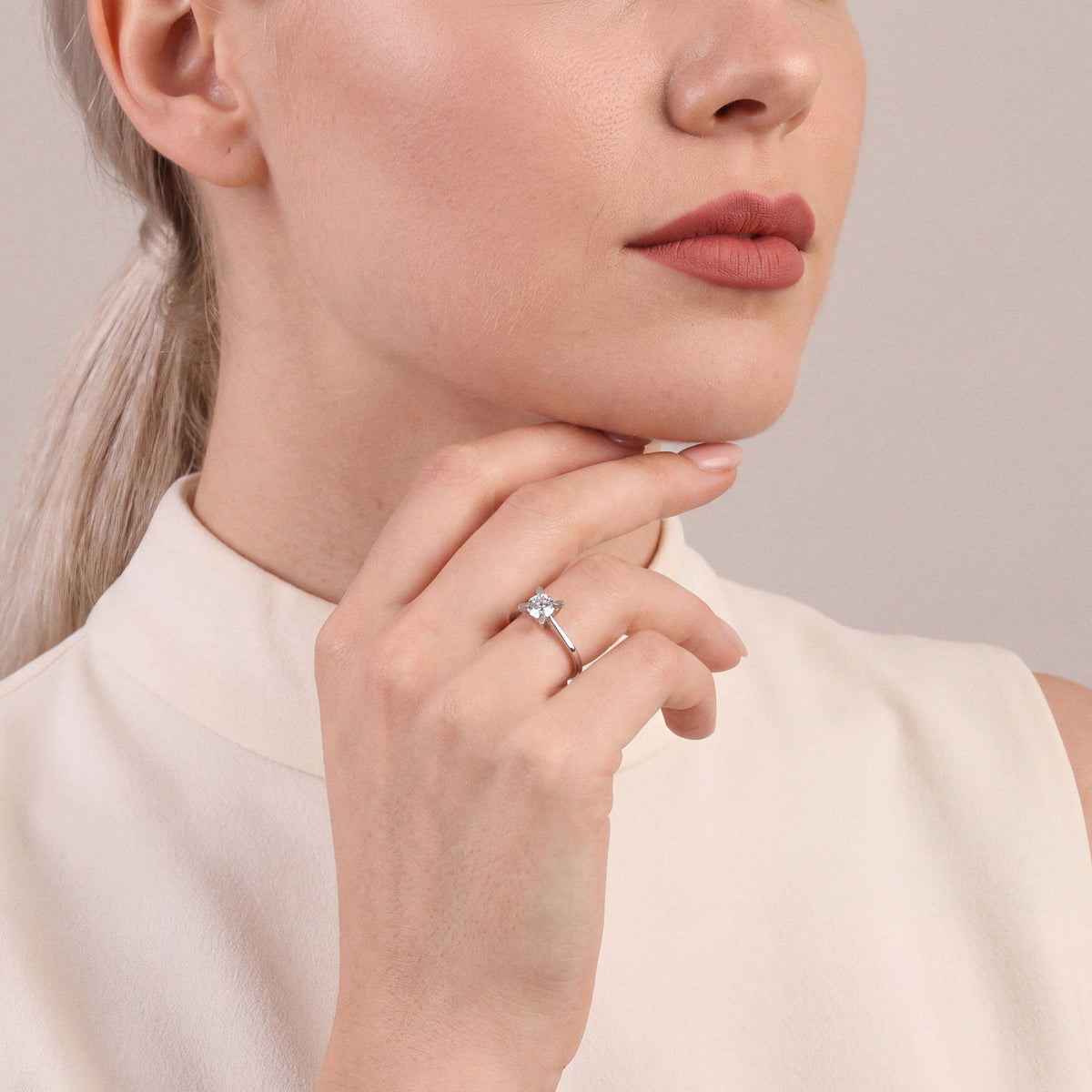 Woman in an ivory high-collar top wearing a 0.60 ct natural diamond solitaire ring in 14K white gold, hand curled under the chin