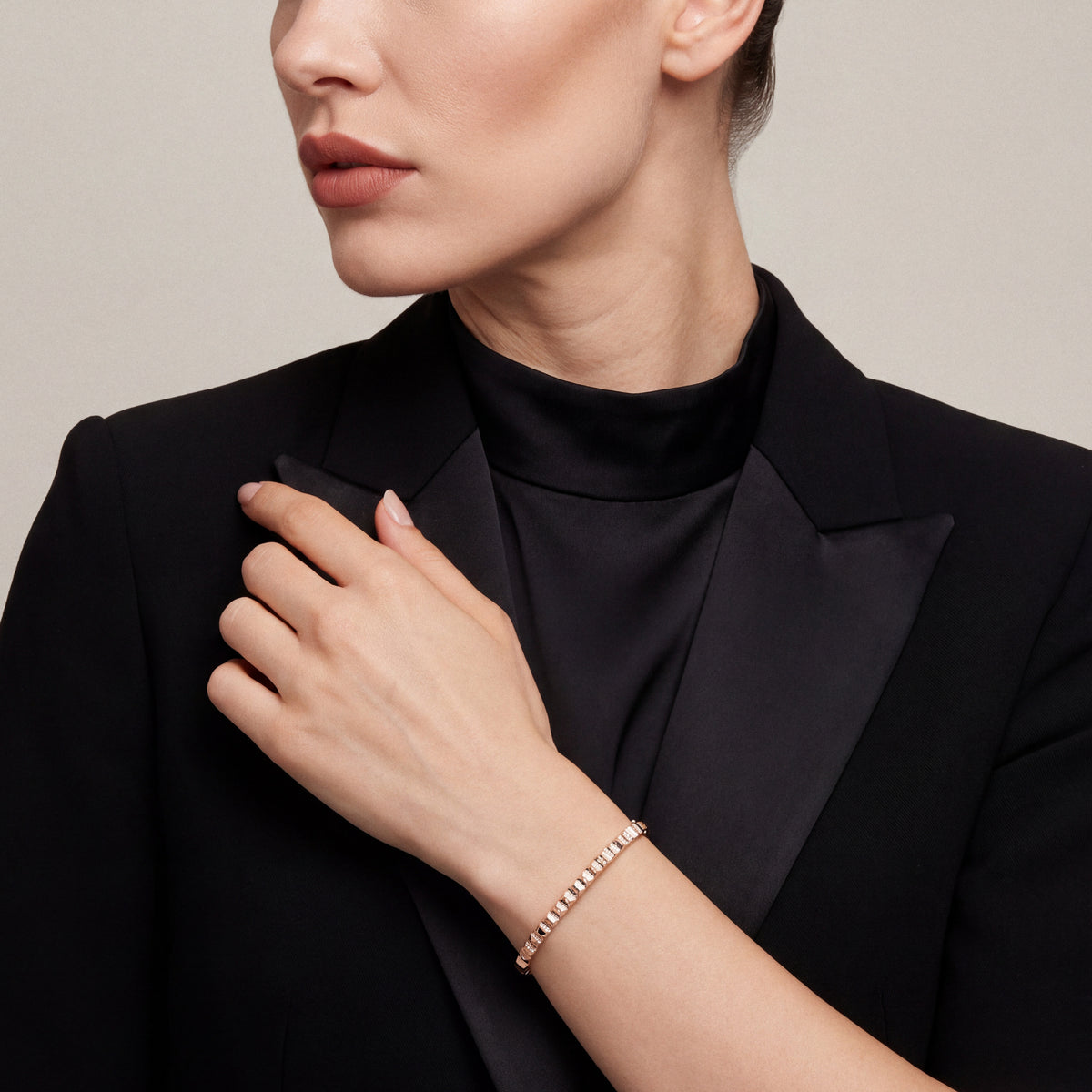 Woman in a black satin-lapel tuxedo jacket wearing a natural diamond pyramid bangle in 14K rose gold, fingertips at the lapel