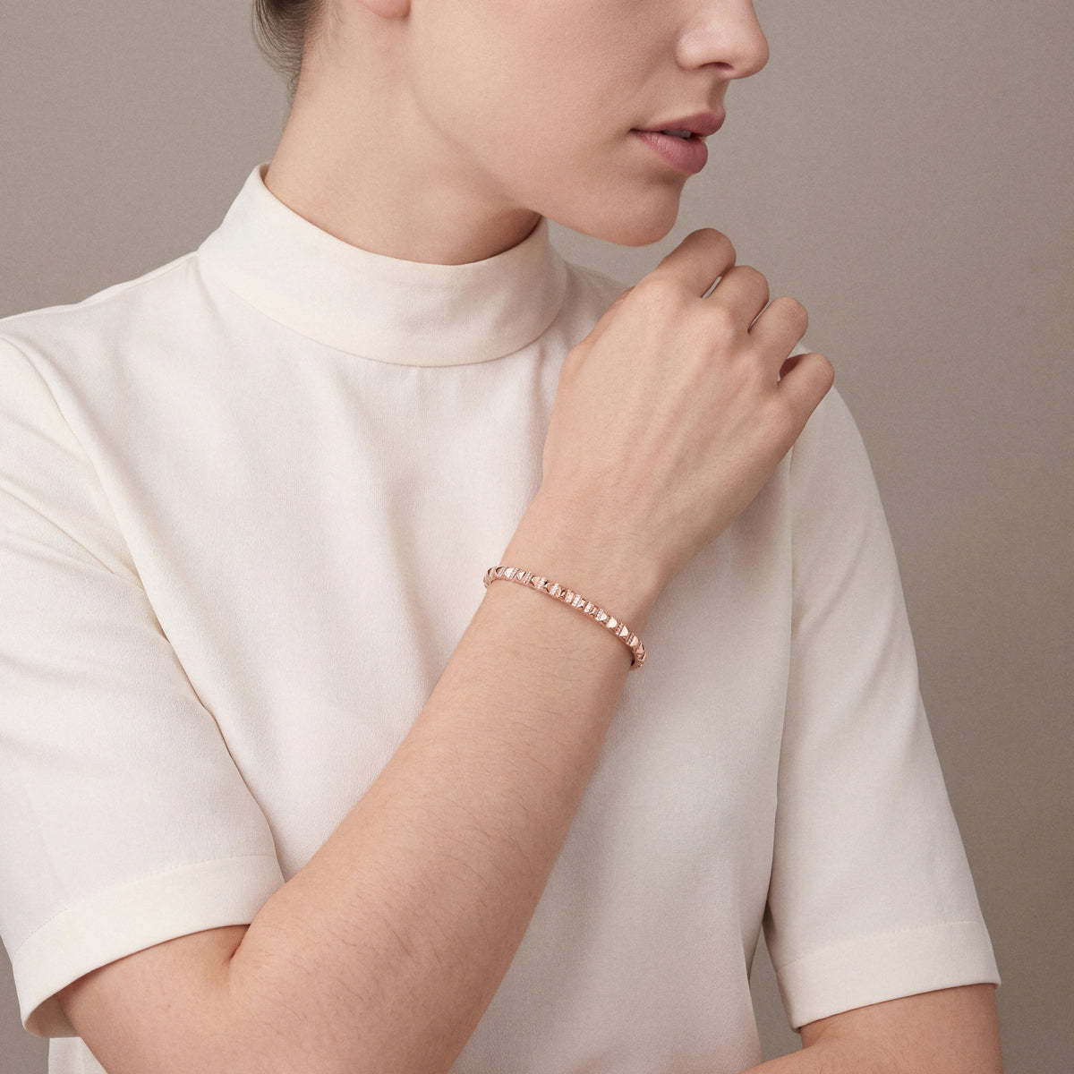 Woman in an ivory high-collar silk top wearing a natural diamond pyramid bangle in 14K rose gold, hand at the opposite shoulder
