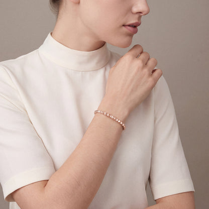 Woman in an ivory high-collar silk top wearing a natural diamond pyramid bangle in 14K rose gold, hand at the opposite shoulder