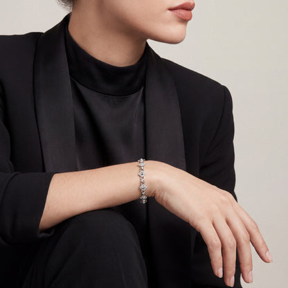 Woman in a black tuxedo jacket, forearm resting on her knee, wearing a 0.92 ct natural diamond pyramid station link bracelet in 14K white gold