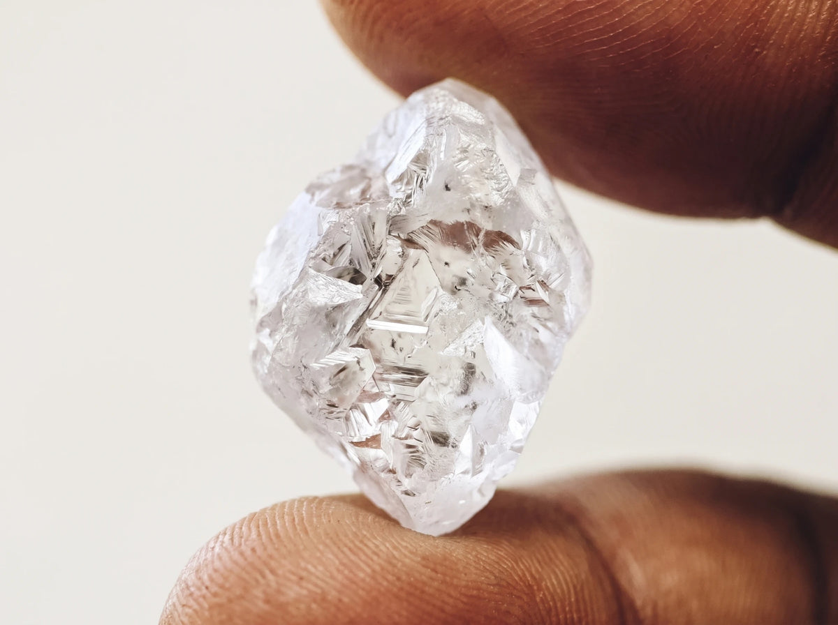 A rough natural diamond crystal held between two fingertips