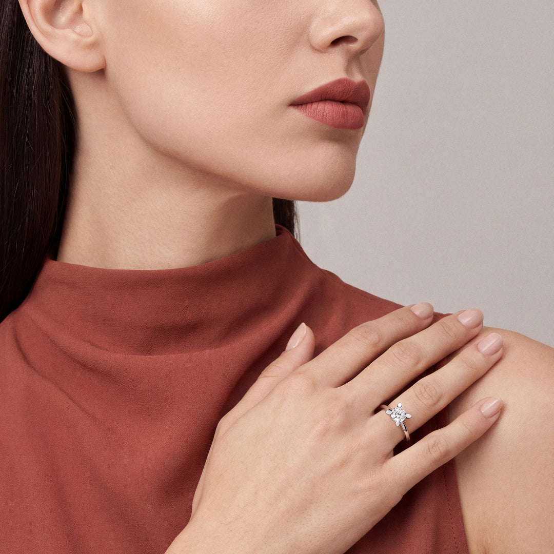 0.60 ct natural round diamond solitaire ring in 14K white gold worn on the ring finger, hand resting on the shoulder of a rust silk mock-neck top