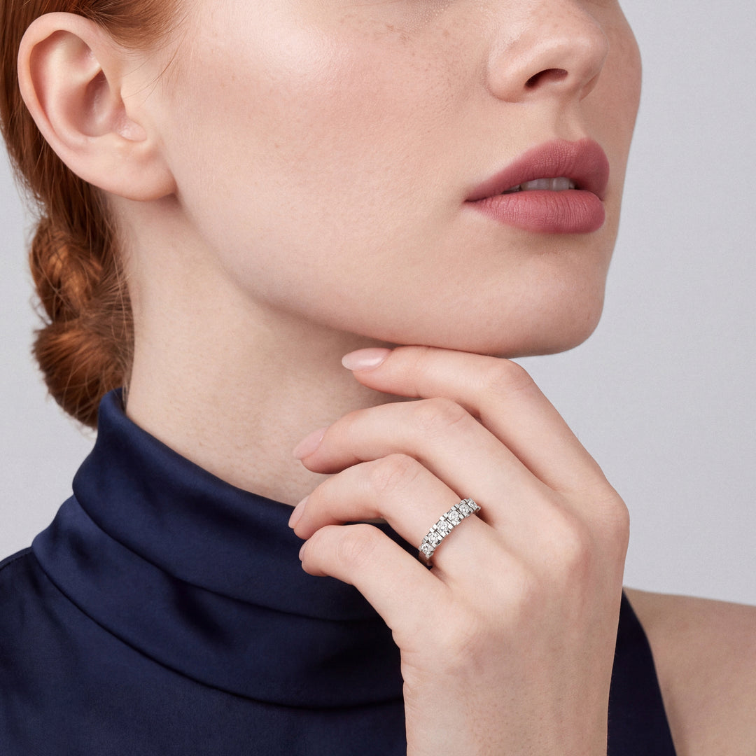 0.65 ct natural diamond half eternity ring in 14K white gold worn on the ring finger, fingers curled at the chin, navy satin high-neck top