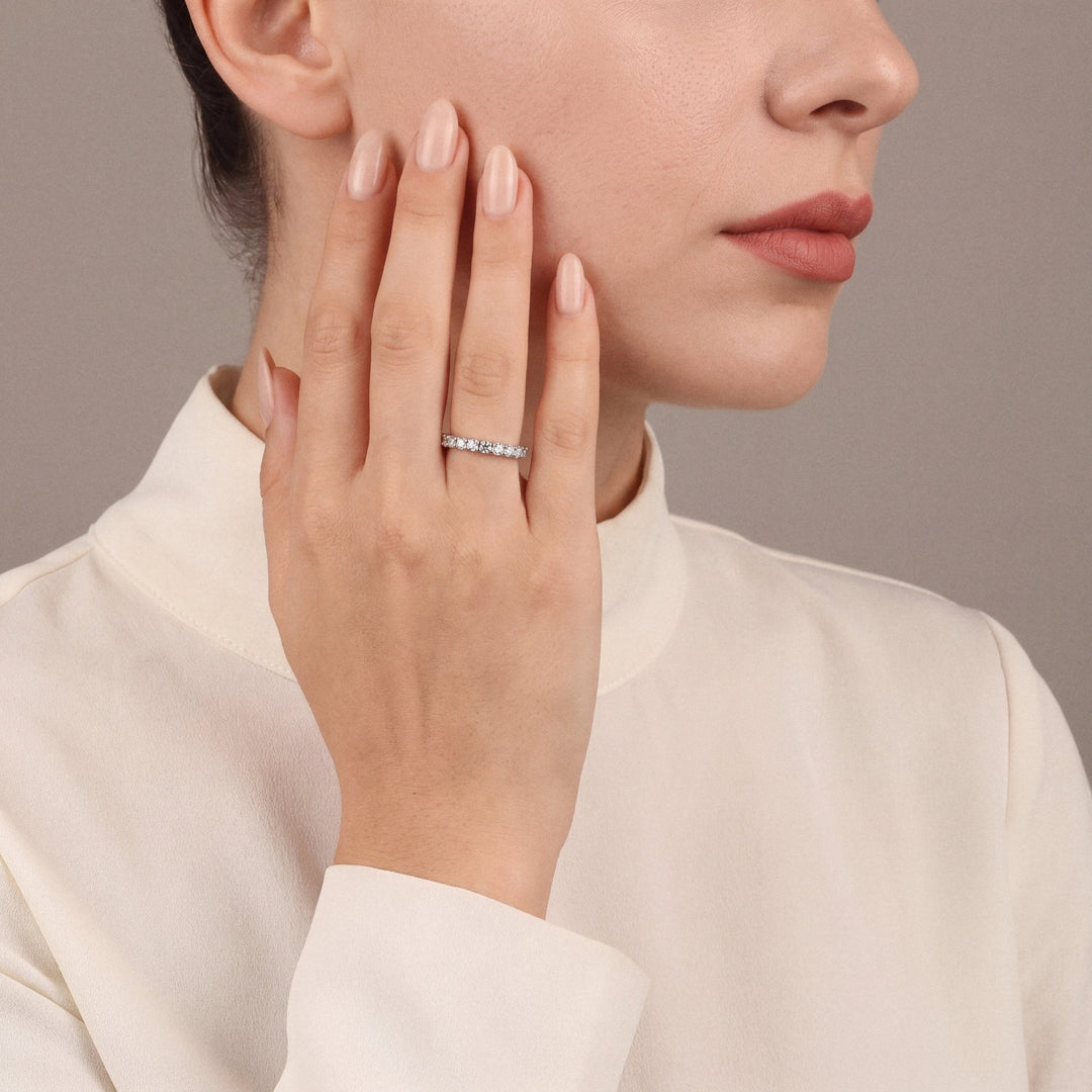 Model in an ivory silk high-neck blouse wearing a natural diamond full eternity ring in 14K white gold, hand on her cheek