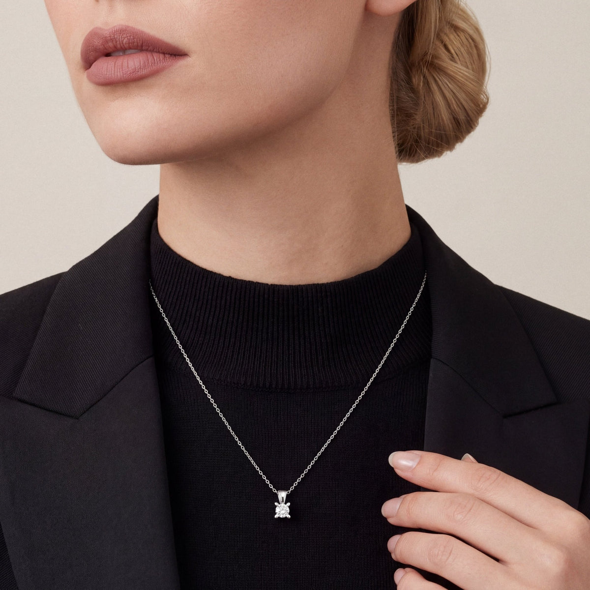 Woman in a black tuxedo jacket and black mock-neck top wearing a 0.50 ct natural diamond solitaire pendant necklace in 14K white gold
