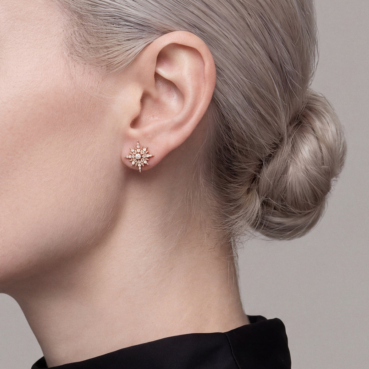 Woman in a black funnel neck wearing a natural diamond starburst stud earring in 14K rose gold, side profile