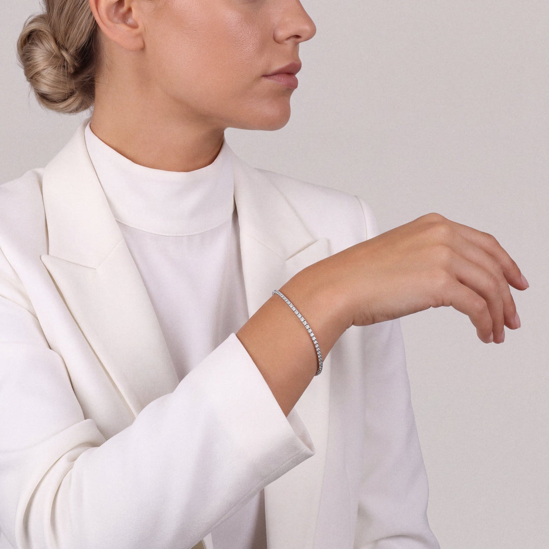 Woman in a white tailored blazer wearing a natural diamond tennis bracelet in 14K white gold, forearm raised
