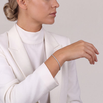 Woman in a white tailored blazer wearing a natural diamond tennis bracelet in 14K white gold, forearm raised