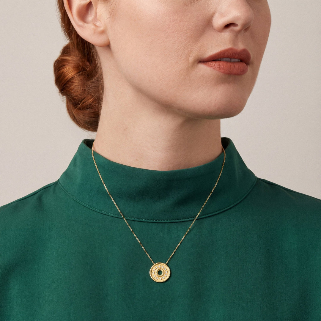 Woman in an emerald silk-crepe funnel-neck top wearing a natural diamond coin disc pendant necklace in 18K yellow gold