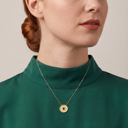 Woman in an emerald silk-crepe funnel-neck top wearing a natural diamond coin disc pendant necklace in 18K yellow gold