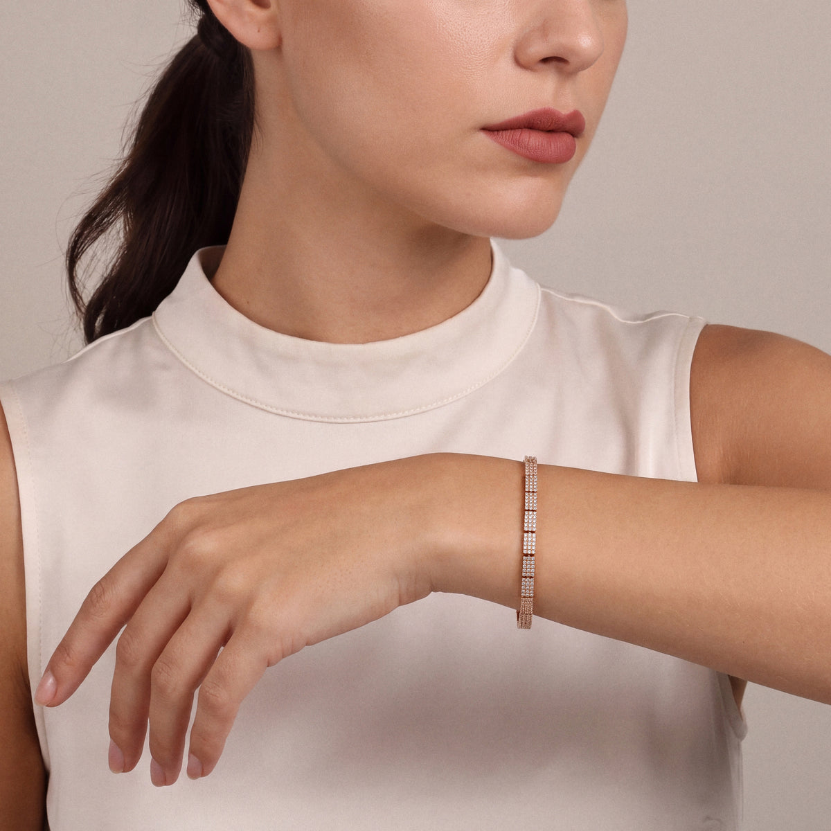 Woman in an ivory satin stand-collar top wearing a natural diamond pavé link bracelet in 14K rose gold, forearm raised across, hand relaxed