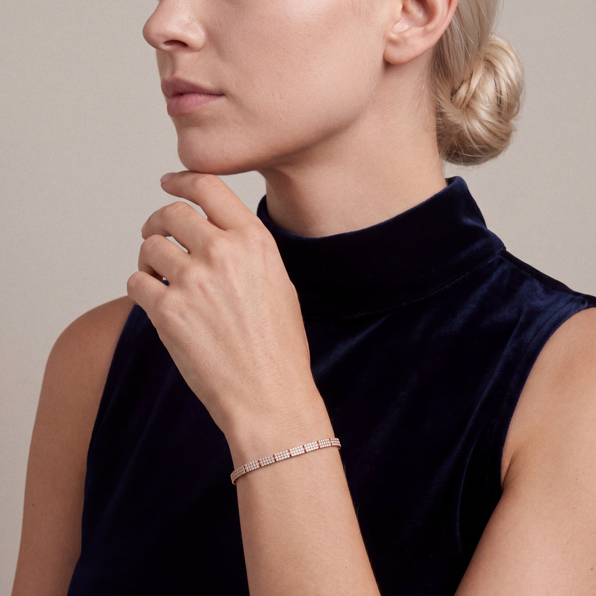 Woman in a navy velvet sleeveless funnel-neck top wearing a natural diamond pavé link bracelet in 14K rose gold, fingertips under the chin