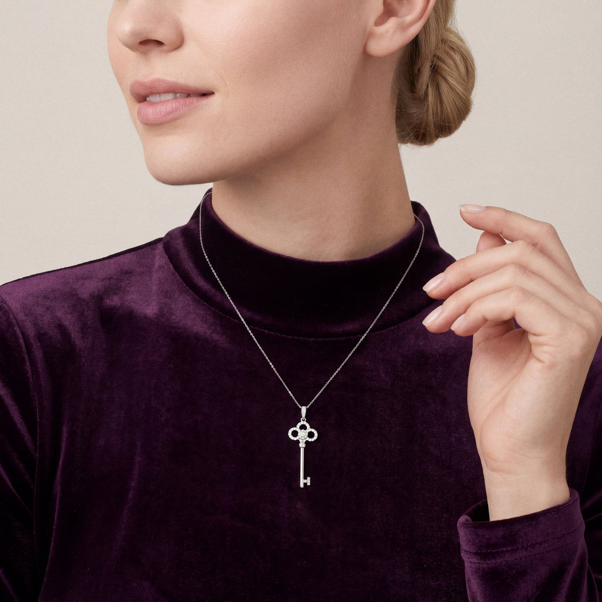 Woman in a plum velvet mock-neck top wearing a natural diamond trefoil key pendant necklace in 14K white gold