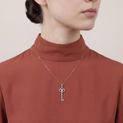 Woman in a rust silk-crepe funnel-neck top wearing a natural diamond trefoil key pendant necklace in 14K white gold