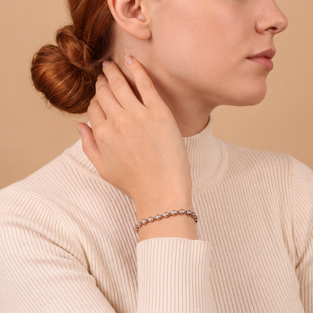 Woman in a cream ribbed turtleneck wearing a natural diamond rose gold link bracelet, hand at the neck