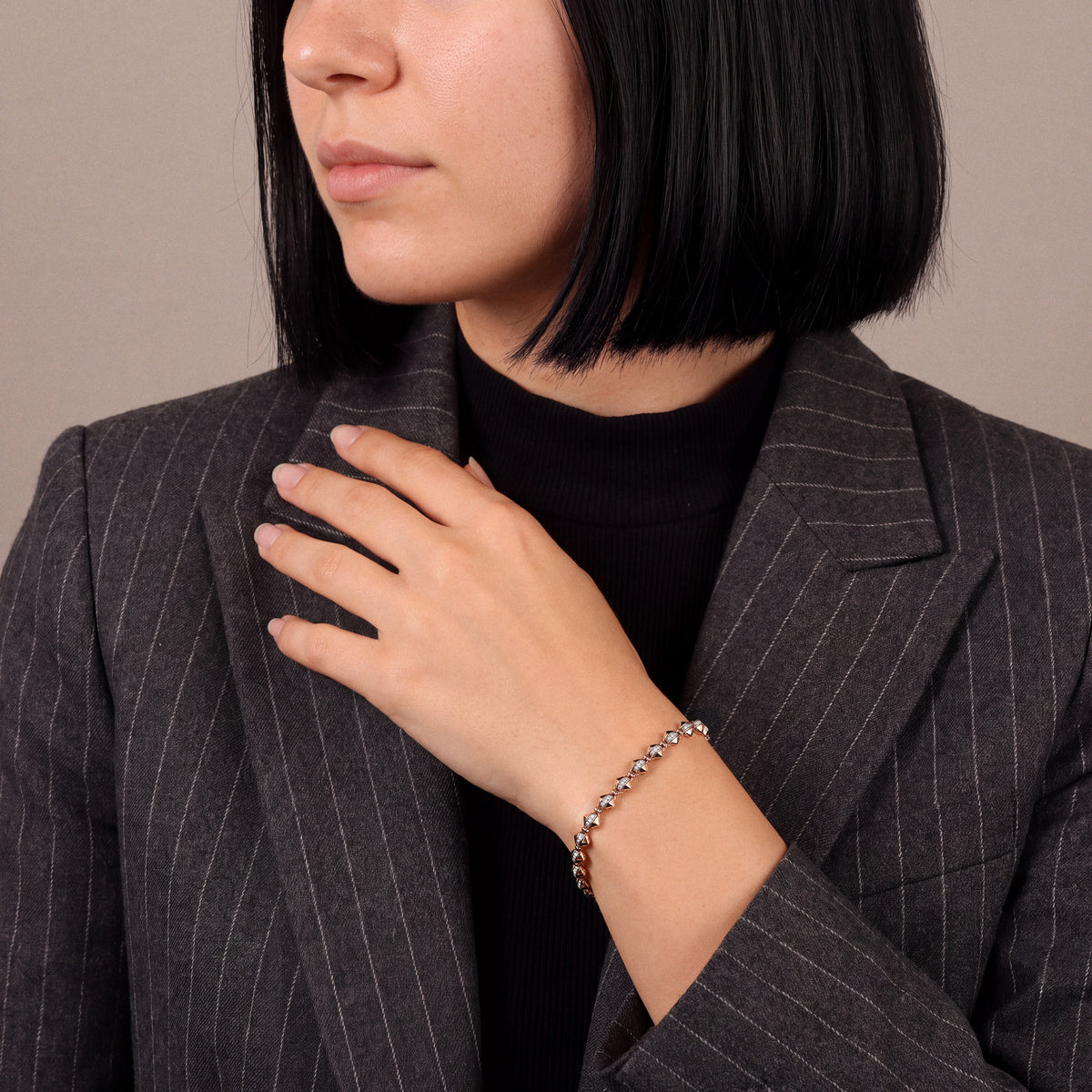 Woman in a charcoal pinstripe blazer wearing a natural diamond rose gold link bracelet, hand at the lapel