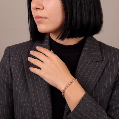 Woman in a charcoal pinstripe blazer wearing a natural diamond rose gold link bracelet, hand at the lapel