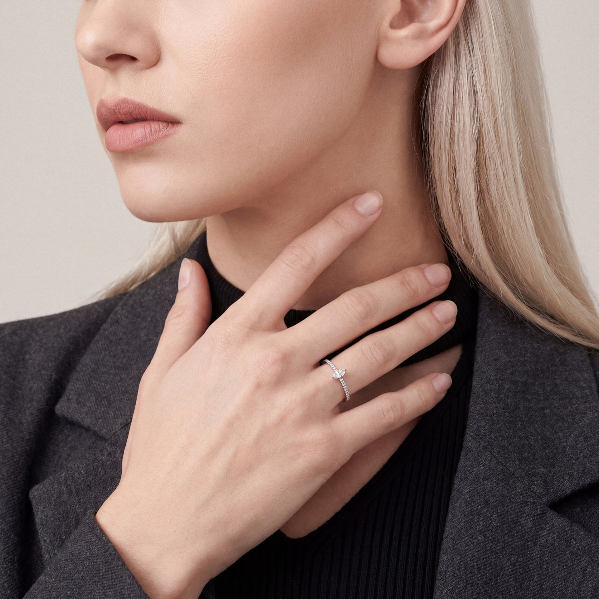 Woman in a charcoal blazer wearing a natural marquise diamond solitaire ring, fingertips at the neck