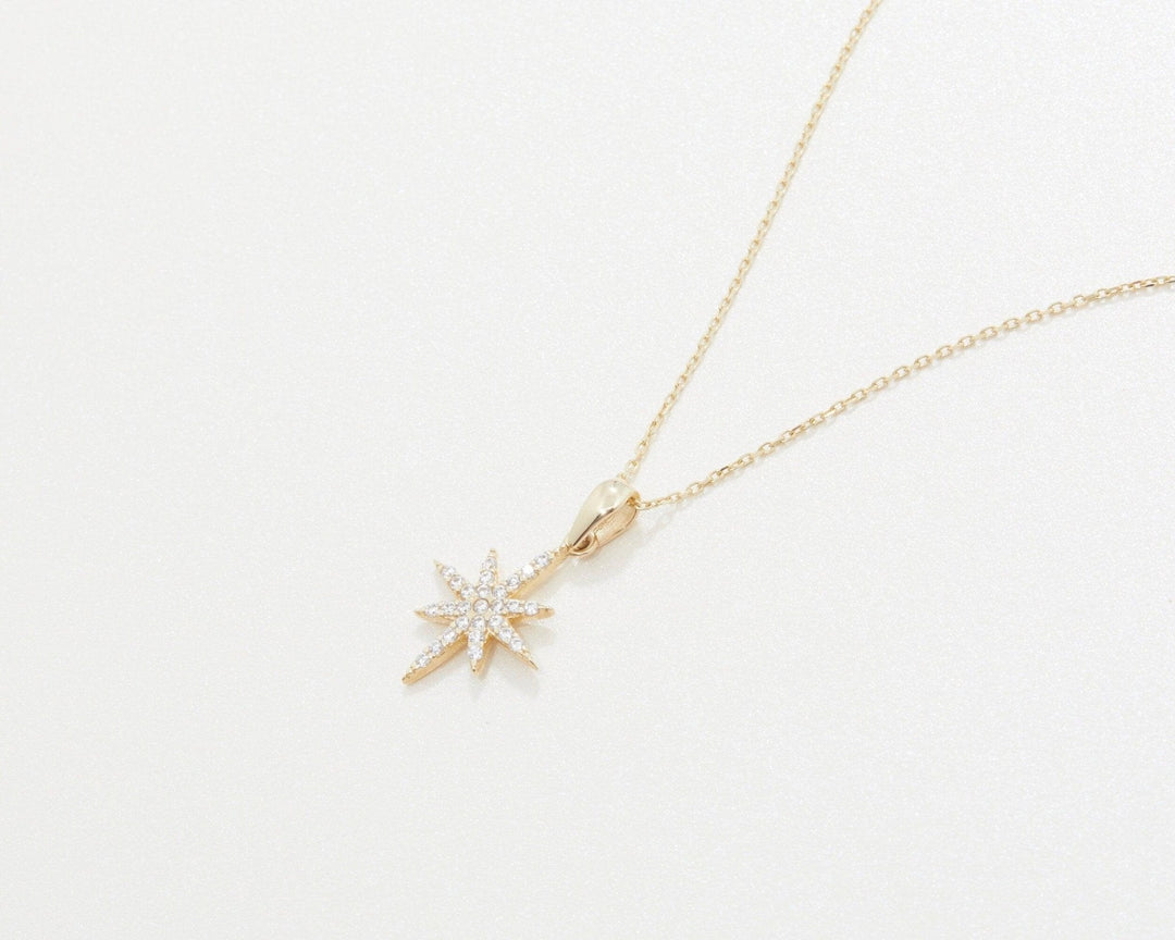 The North Star Necklace in 14K solid gold laid flat, showing the star and its bail.