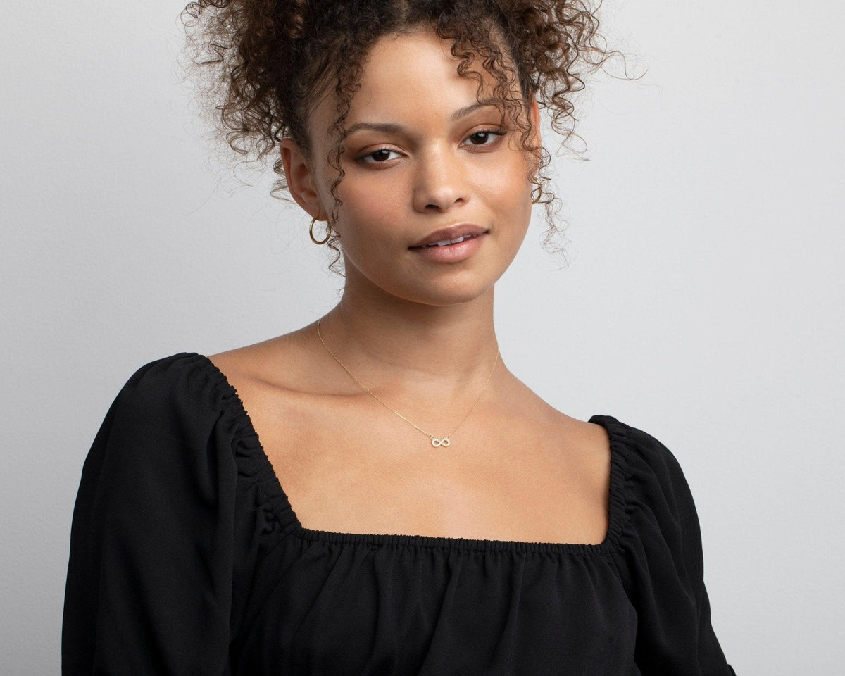 The 14K solid gold pavé infinity necklace on a model in a black square-neck top.