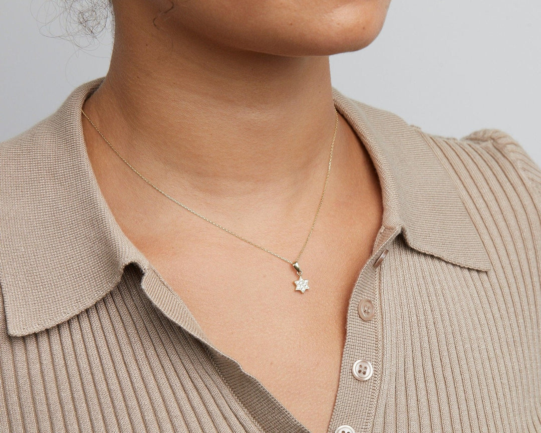 Close-up of the pavé Star of David necklace in 14K solid gold, hanging in the open collar of a knit top.