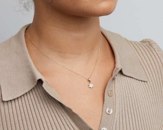 Close-up of the pavé Star of David necklace in 14K solid gold, hanging in the open collar of a knit top.
