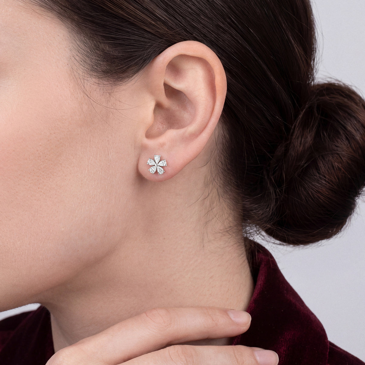 Woman in a burgundy velvet jacket wearing a pear-cut natural diamond flower stud earring in 14K white gold