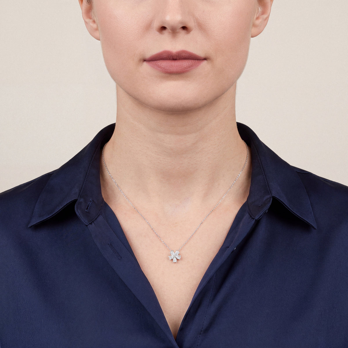 Woman in a navy silk shirt wearing the pear-cut natural diamond flower pendant necklace in 14K white gold